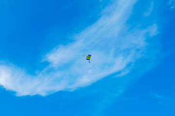 Naklejka na ściany i meble Male skydiver flies under the wing of the parachute, descending and coming in to land closer to the ground on a background of blue sky, white clouds