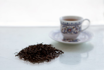 Dry leafs of black chinese tea and teacup on a white background