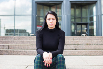 Young business woman in black shirt during the break, sat down on the steps in front of modern building