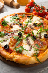 Pizza con mozzarella, pomodoro, acciughe, rucola e olive nere