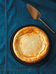 Plate with whole cheesecake pie on table with jeans tablecloth. Classic cheesecake flat lay or top view. Vertical.