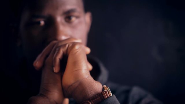 Pensive serious young american african man staring at camera in the darkness