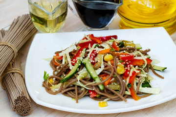 Vietnamese vegetarian salad with buckwheat noodles, carrots cucumbers, red pepper and sesame seeds, macro on a plate. Asian food. Soba noodles with sesame seeds and mixed vegetables. Healthy food.