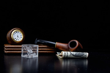 Table set with a clock and a number of smoking pipe lies on the dollar and euro bills. Glass cube with a mobile phone icon. Concept - business without vacation