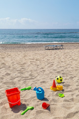 Fototapeta na wymiar children's toys on the beach sand against turquoise sea.