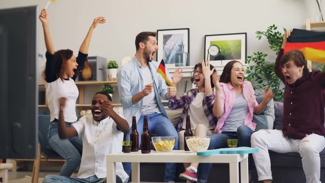 Cheerful Germans are watching sports at home on TV holding German official flags having fun doing high-five and hugging. Television, leisure and fans concept.