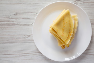Pile of tasty blini on a white plate over white wooden background, top view. Flat lay, overhead,...