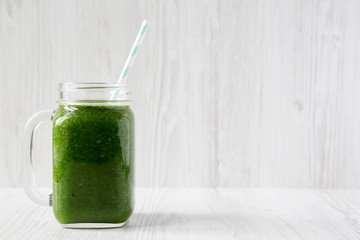 Green smoothie with spinach, avocado and banana in glass jars on a white wooden surface, side view. Copy space.