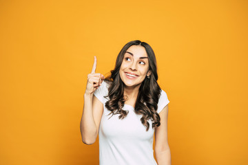 Idea! Pretty girl with nice hairstyle and gorgeous smile in white T-shirt is holding her finger pointed up which is telling about her genius idea.