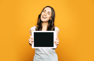 A screen of a white tablet PC which is placed in hands of  a nice and happy woman with pleasant appearance and cool casual outfit.