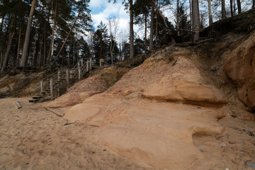 Limestone beach at the Baltic Sea with beautiful sand pattern and vivid red and orange color - Tourist writings on the walls and rocks and sand - Veczemju Klintis, Latvia - April 13, 2019