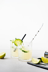 Two glasses with Fresh Summer Healthy homemade mojito lemonade or cocktail with cucumber garnished with slice lime and micro greens on light background.