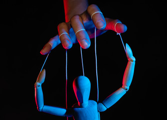 Concept of control. Marionette in human hand. Objects are colored on red and blue light.