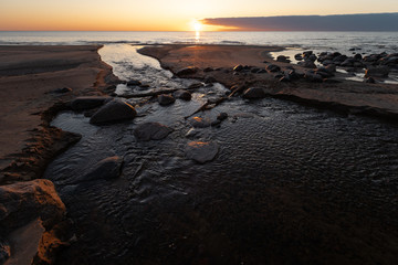 Beautiful sunset with red sand and spring water from a river exiting to the sea - Veczemju Klintis, Latvia - April 13, 2019