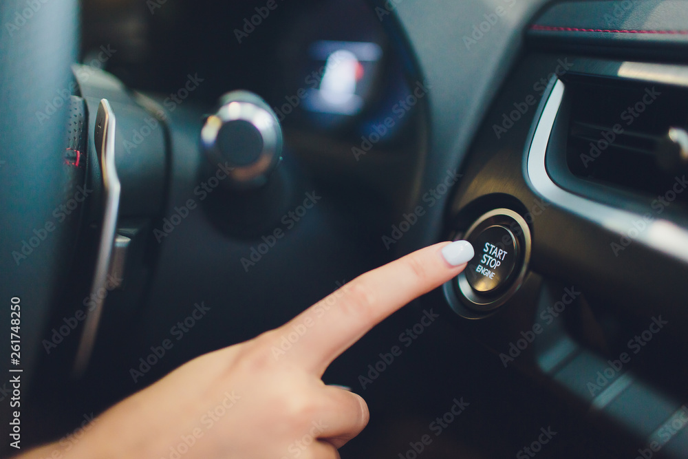 Wall mural Car driver starting the engine keyless. Black. female hand.