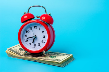 Red retro styled alarm clock on heap of american dollars.