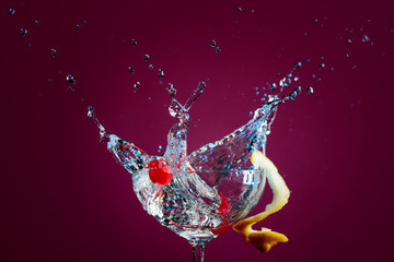 Colorful cocktail in glass with splashes garnished with lemon and cherries.