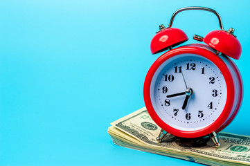 Red retro styled alarm clock on heap of american dollars.