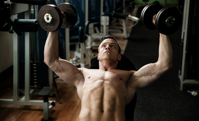 phisique fitness competitor works out in gym lifting dumbbells