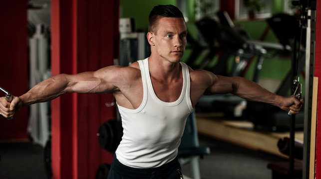 phisique fitness competitor works out in gym lifting dumbbells