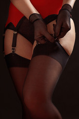 Woman fastens black stockings to the erotic garter belt on a black background close up