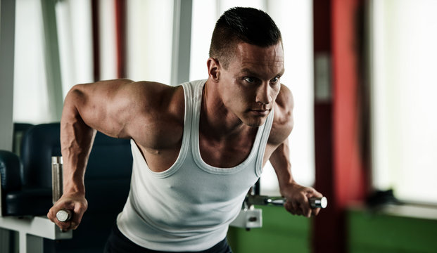 phisique fitness competitor works out in gym lifting dumbbells