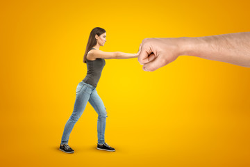 Fototapeta na wymiar Young brunette girl wearing casual jeans and t-shirt making stop gesture against big male stretched fist on yellow background