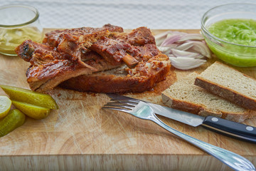 Grilled tasty and spicy bbq spare ribs marinated and served on wooden plate with slices of rustic bread, pickled cucumbers, french style mustard, chopped onion and fresh cucumber salad in glass bowl.
