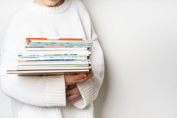 Girl in a white woolen sweater holding a stack of children's books on white background with copy...