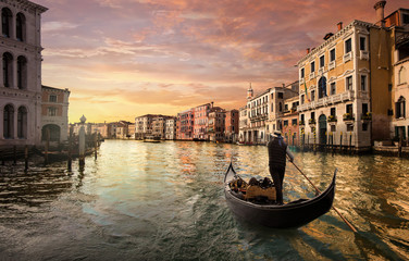 A gondolier is driving his gondola in the grand canal at sunset in Venice, Italy. - obrazy, fototapety, plakaty