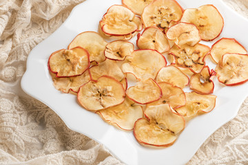 Apple chips on white figured square plate on lace fabric.