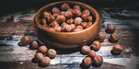 Banner. Hazelnuts nuts in a wooden bowl on a dark background. Low key lighting.