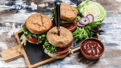 Fototapeta na wymiar Homemade burgers with beef, tomatoes, lettuce, cheese and spicy tomato sauce on a cutting board.