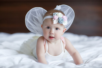 Blue-eyed baby with angel wings behind him.Baby Newborn with Angel Wings. Child Sitting at Blue Sky Cloud. Girl 5-7 months sitting on a white bed in the bedroom.Cute newborn angel