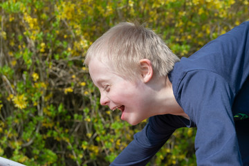   Defect,childcare,medicine and people concept: Blond boy with down syndrome playing in a park at spring time.