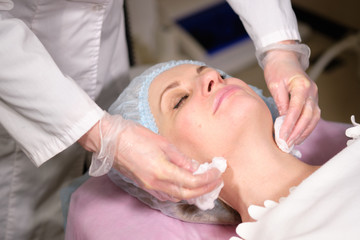 Fototapeta na wymiar Cosmetologist remove a face mask to her patient . Anti-ageing and smoothing procedure in a beauty salon. Doctor in a cosmetological clinic making a treatment of skin care