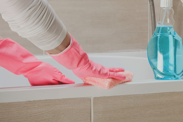 Housemaid in the rubber gloves cleaning bathroom with a sponge