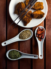CLOSE UP OF CHICKEN NUGGETS NEXT TO SPOONS WITH SPICES AND METAL SPIKE