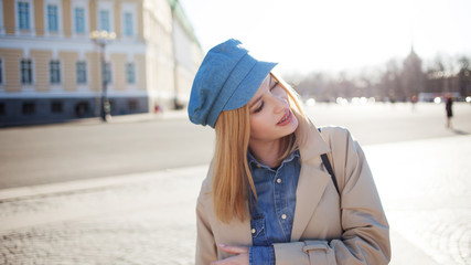 Stylish young blonde in denim cap and beige raincoat. Beautiful young woman