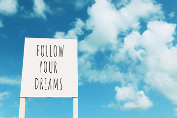 sign against blue sky with clouds with the text – follow your dreams