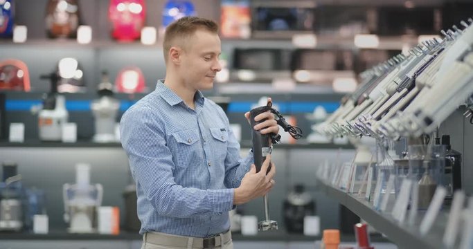 A man chooses a blender in the appliances store kitchen appliances in his hands and considers the design and characteristics