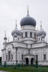 Christian orthodox white church with silver and grey domes with gold crosses. Calm grey sky above