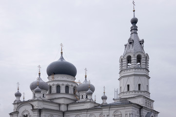 Christian orthodox white church with silver and grey domes with gold crosses. Calm grey sky above