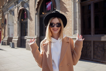 Happy girl outdoors, Sunny day. Fashionable and trendy young woman in black felt hat and stylish beige coat