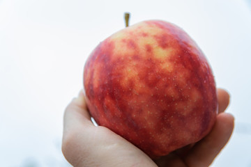  Large,ripe,colorful mottled apple in the hand of a man on a  bright window.