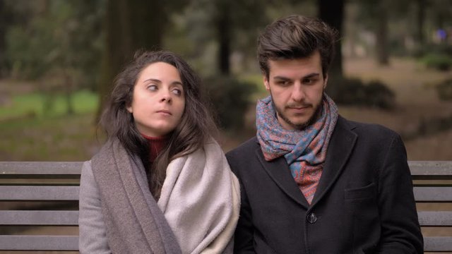 Shy young couple flirting and kissing sitting on park bench. First date