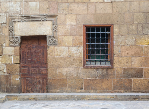 Background of old stone bricks wall with grunge wooden closed door and window with iron grid, Cairo, Egypt