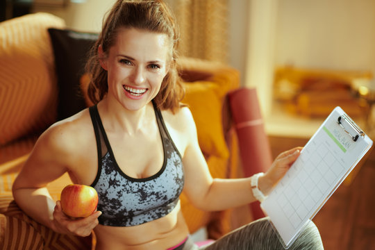 happy sports woman holding apple and clipboard with meal plan