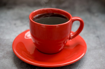Red cup of coffee on a saucer on a black background
