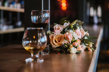 A glass of whiskey, brandy and wine stand on the bar. Behind lies a beautiful bridal bouquet with eucalyptus and roses
